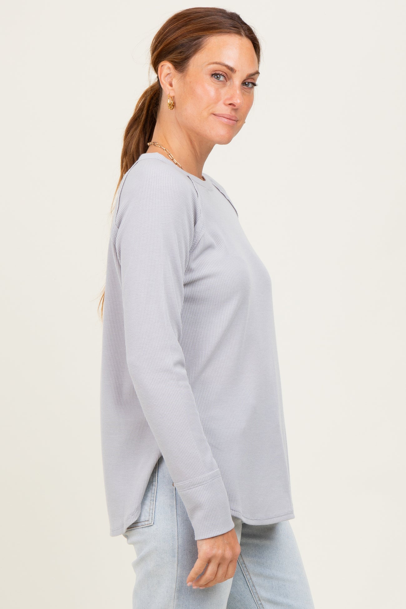 woman wearing a light gray long sleeve ribbed top with side slits and relaxed fit, paired with light blue jeans