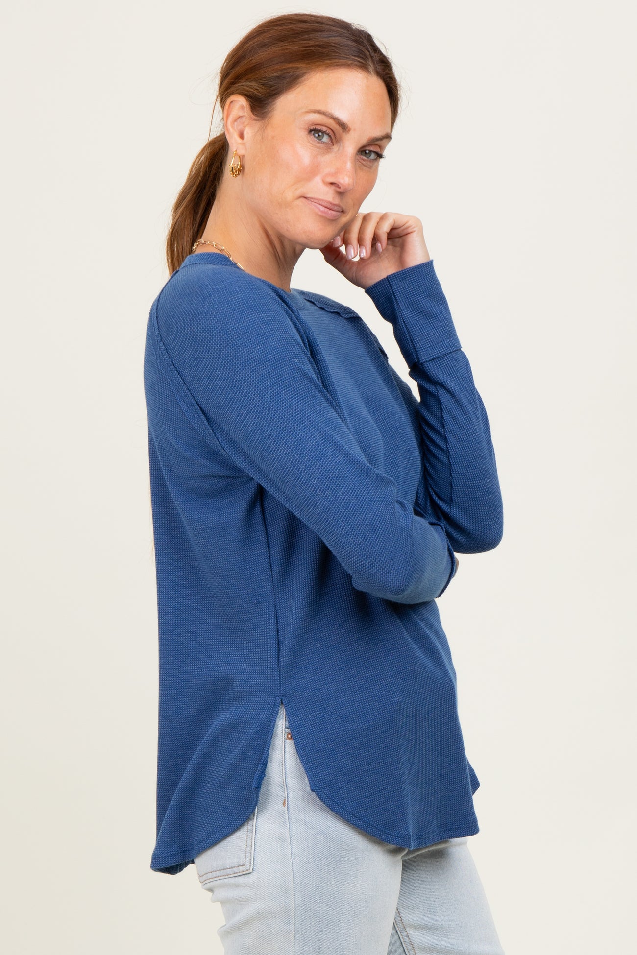 woman wearing a blue long sleeve ribbed top with side slits and a curved hem paired with light denim jeans