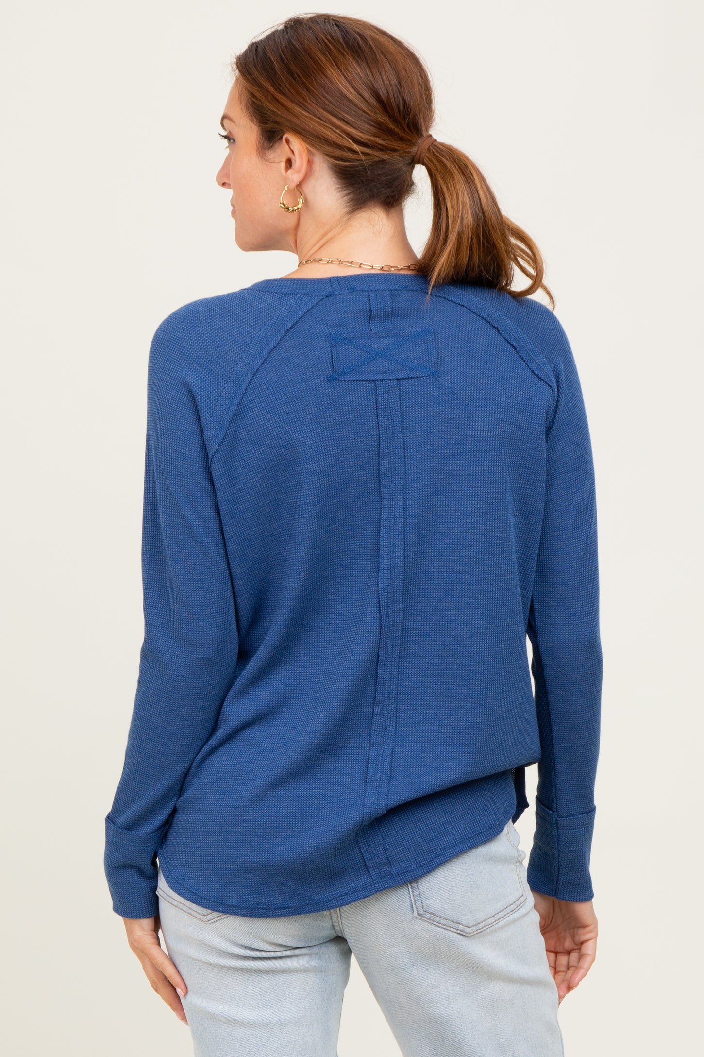 woman wearing a back view of a navy blue long sleeve shirt with a ribbed texture and a split hem detail