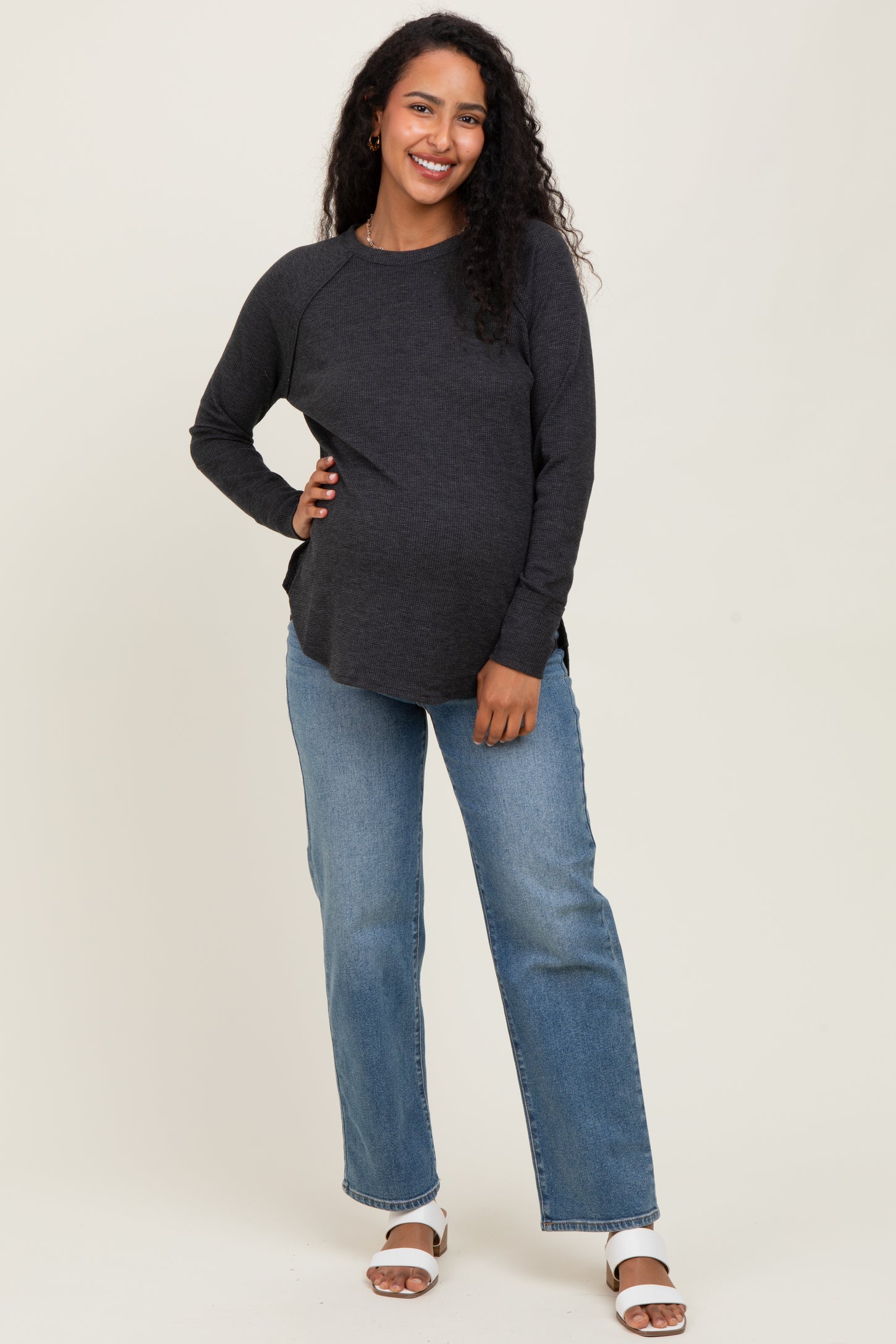 woman wearing a dark gray maternity long sleeve top and showing her baby bump, paired with light blue straight leg jeans