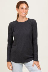 woman wearing a dark gray long sleeve ribbed top with raglan sleeves and a rounded hem, smiling at the camera