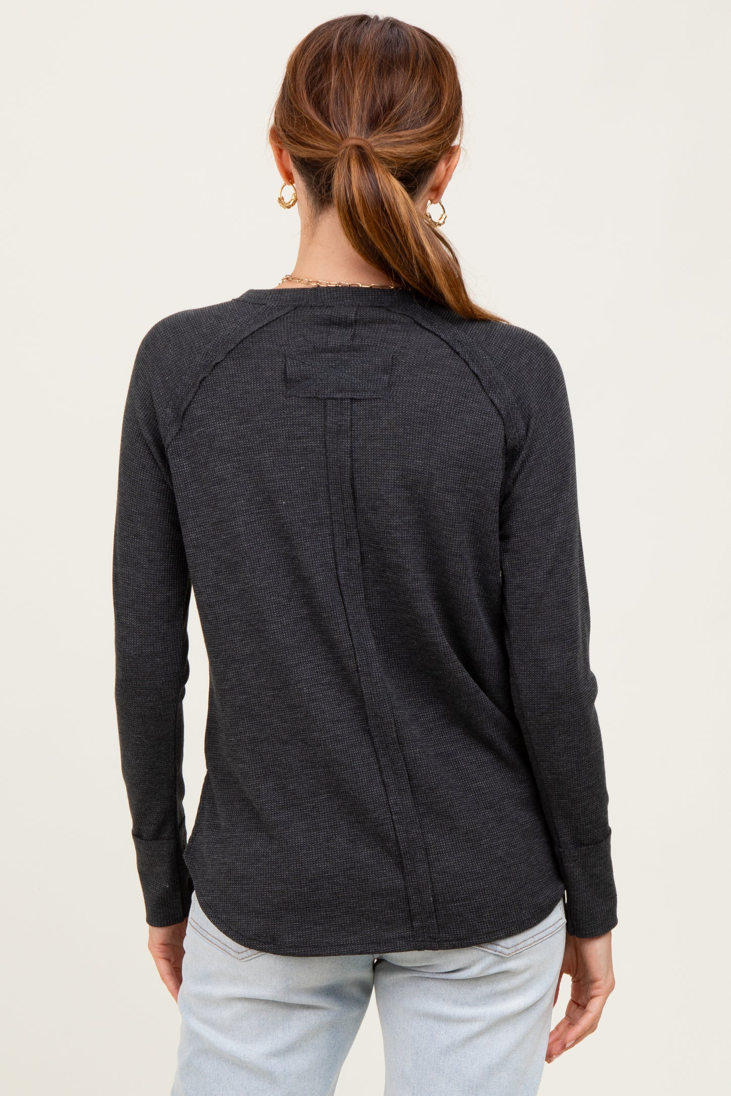 woman wearing a dark gray long sleeve top with a back seam detail and round hemline, seen from the back