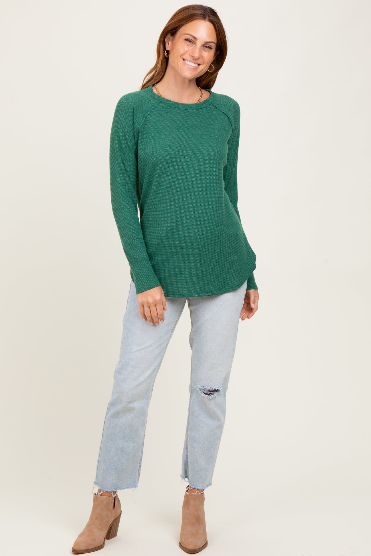 woman wearing a green waffle knit long sleeve top with a curved hem and light blue distressed jeans