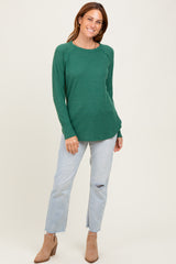 woman wearing a green waffle knit long sleeve top with a curved hem and light blue distressed jeans