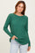woman wearing a green ribbed long sleeve top with a relaxed fit and side slits, posing with one hand in her pocket