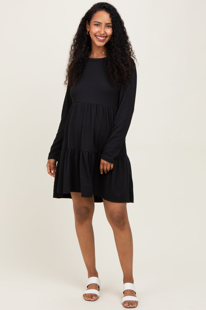 woman wearing a black long sleeve maternity dress with tiered ruffle hem and a visible baby bump