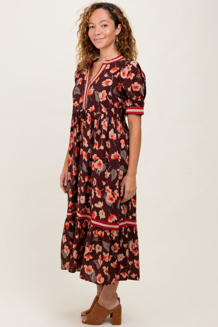 woman wearing a brown floral midi dress with puff sleeves and a v-neckline, standing sideways on a neutral background