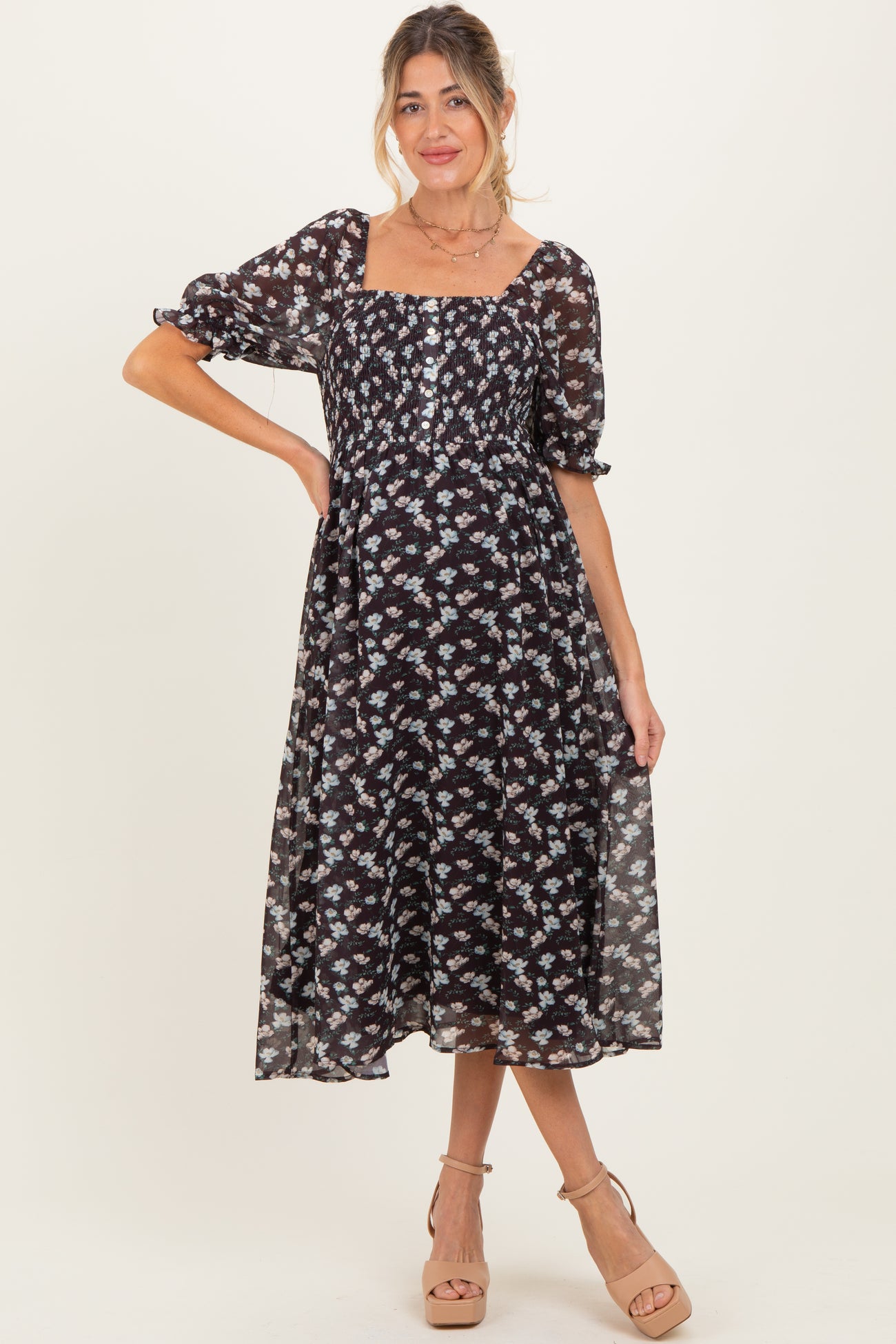 woman wearing a black floral maternity dress with a square neckline and puff sleeves, showing her baby bump