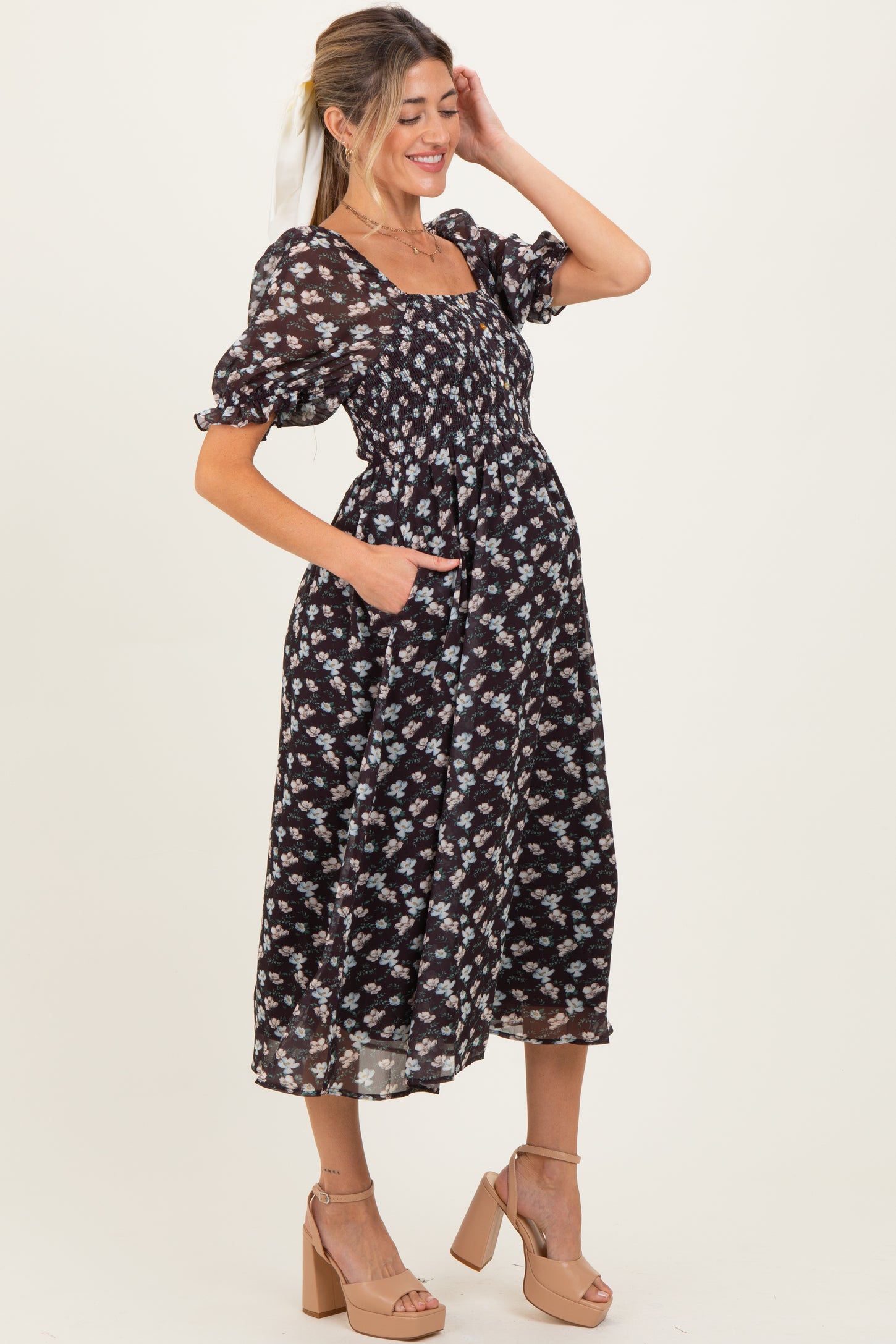 woman wearing a black floral print maternity dress with puffed sleeves and pockets, showcasing her baby bump