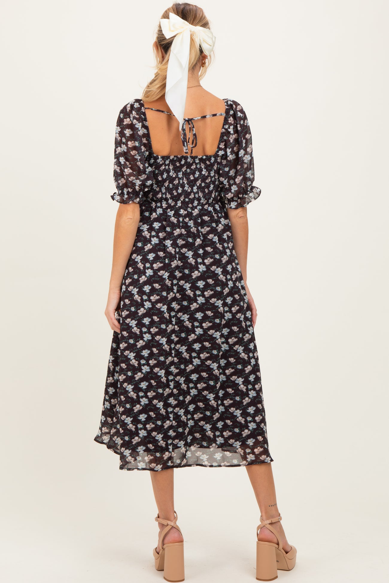 woman wearing a black floral maternity dress with puff sleeves and a tie-back detail, showing a baby bump