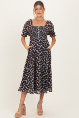 woman wearing a black floral maternity dress with puff sleeves, a square neckline, and pockets, showcasing her baby bump