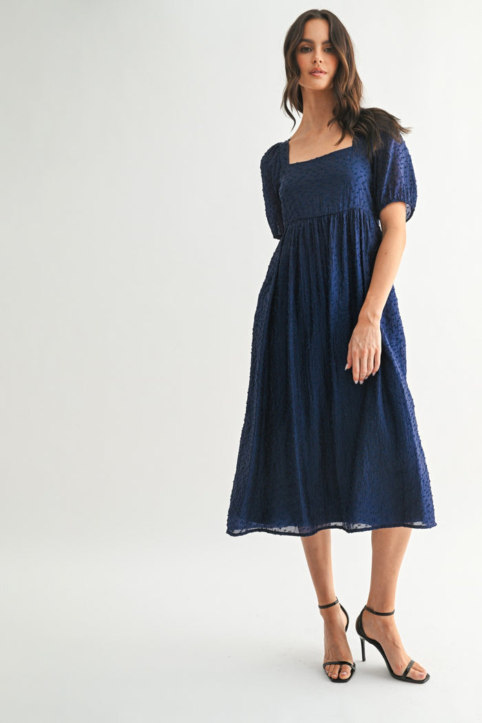woman wearing a navy blue textured midi dress with a square neckline and puff sleeves
