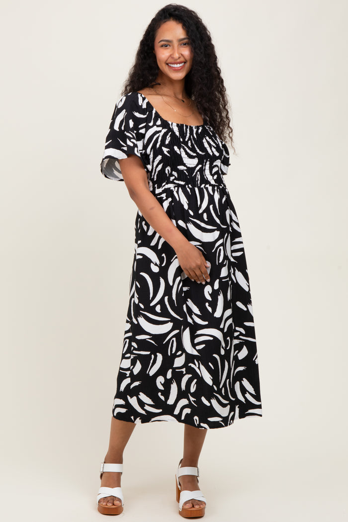 woman wearing a black and white patterned maternity dress with a smocked waist and flutter sleeves, holding her baby bump