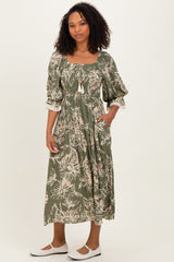 woman wearing a green floral maxi dress with puff sleeves and tie detail, standing with hands in pockets