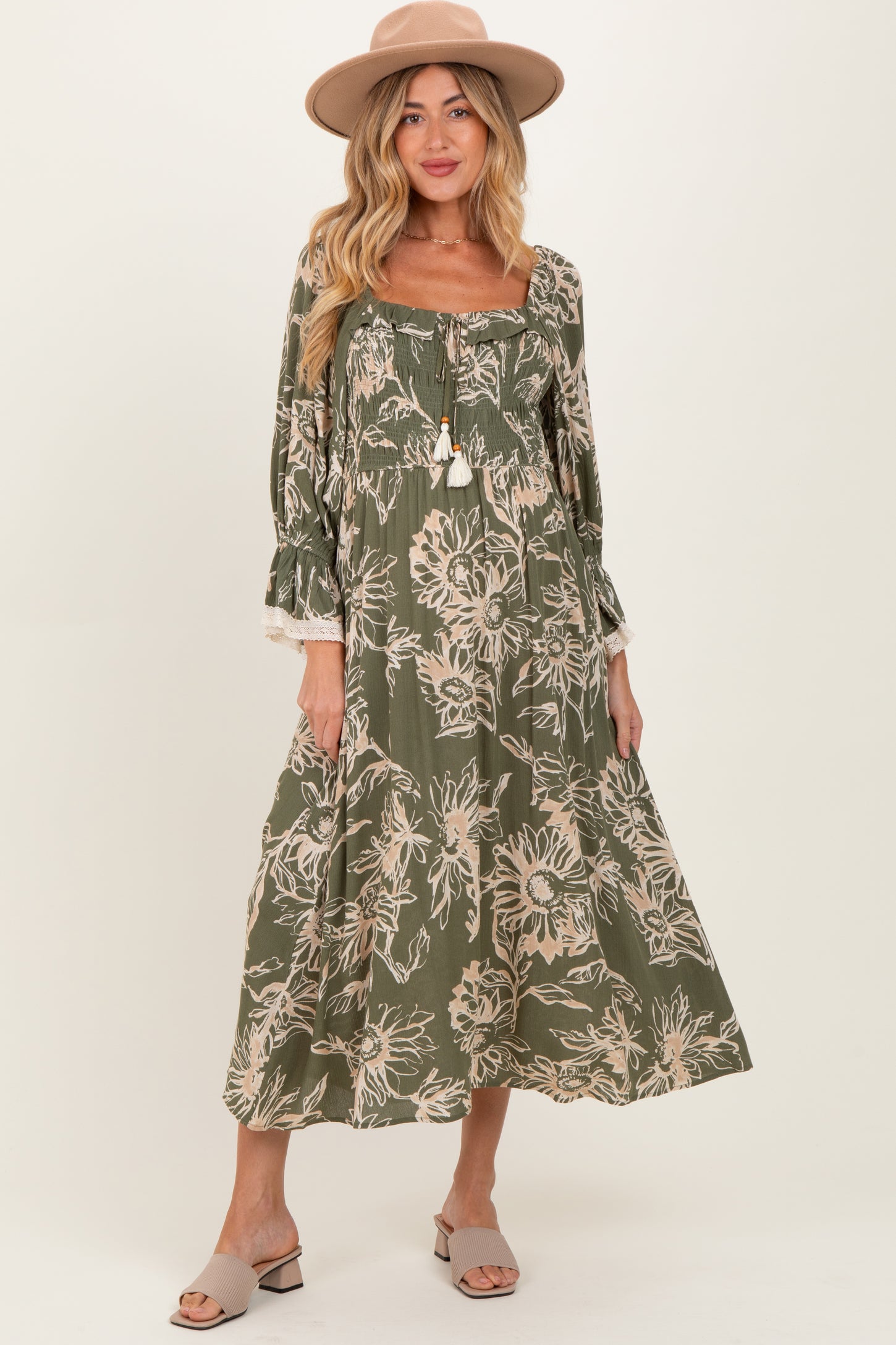 woman wearing a floral print olive green maternity dress with long sleeves and a flowy skirt, accessorized with a hat