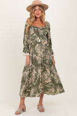 woman wearing a floral print olive green maternity dress with long sleeves and a flowy skirt, accessorized with a hat