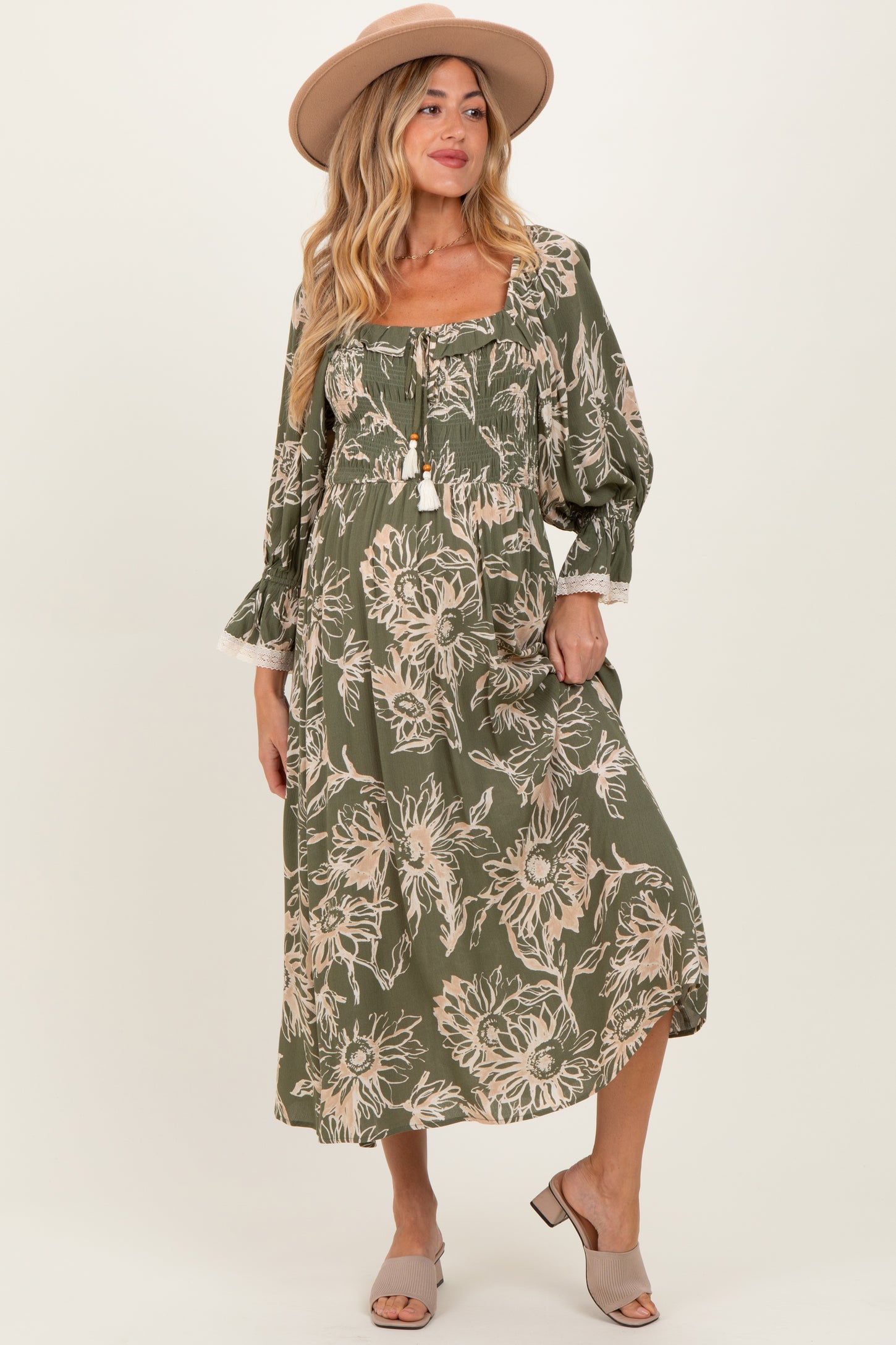 woman wearing a green floral maternity dress with puff sleeves and a tie front, styled with a hat and sandals