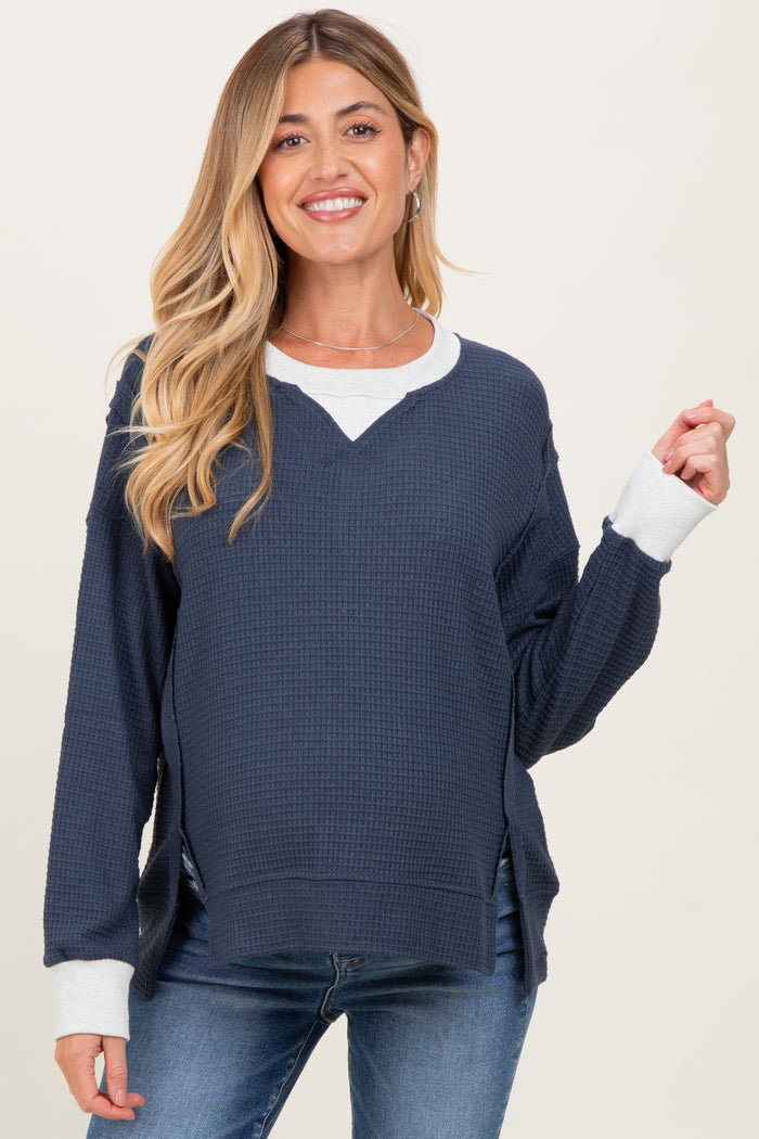 woman wearing a navy blue waffle knit maternity top with light gray trim and side slits, smiling at the camera