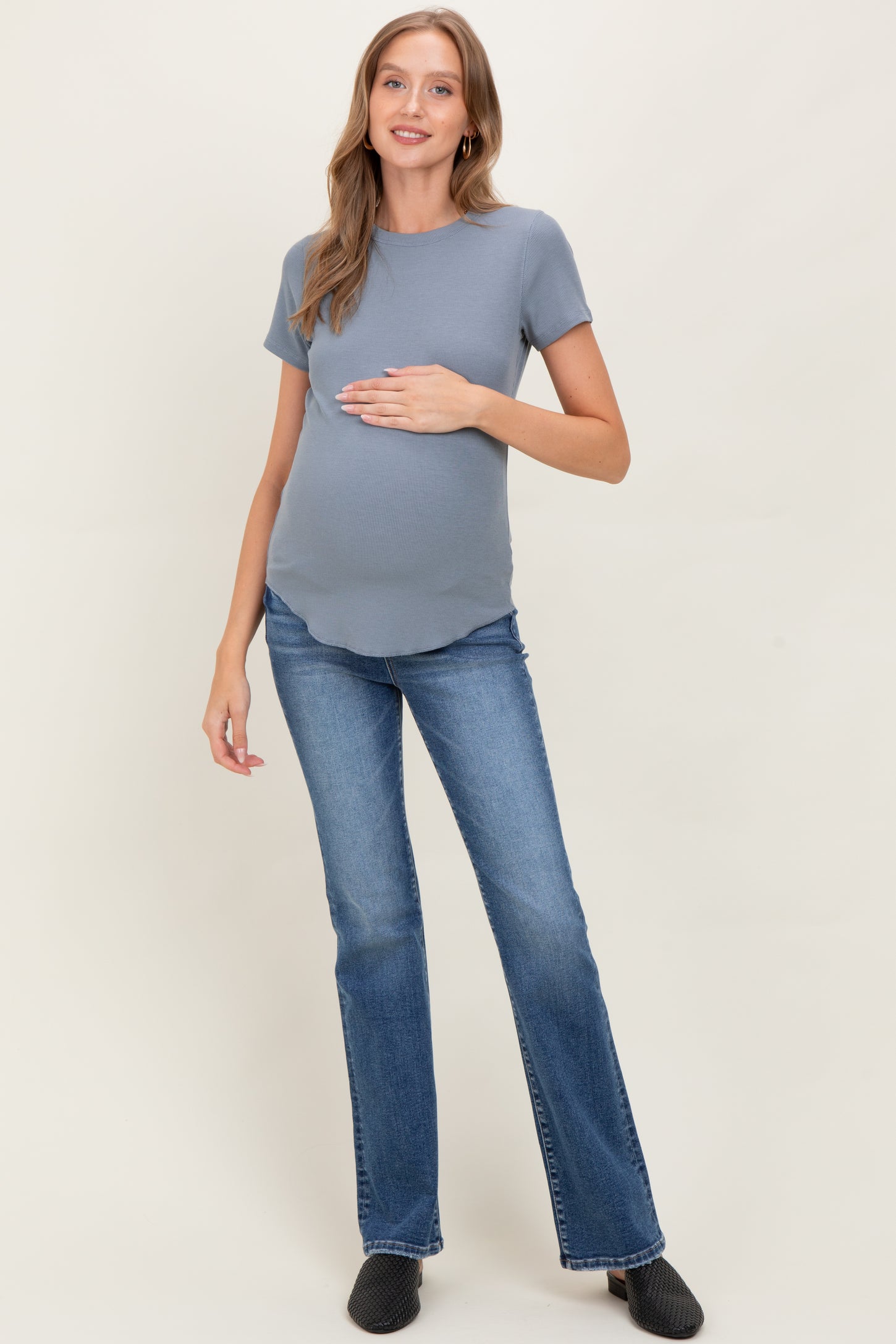 woman wearing a blue short sleeve maternity top and flared jeans, holding her baby bump
