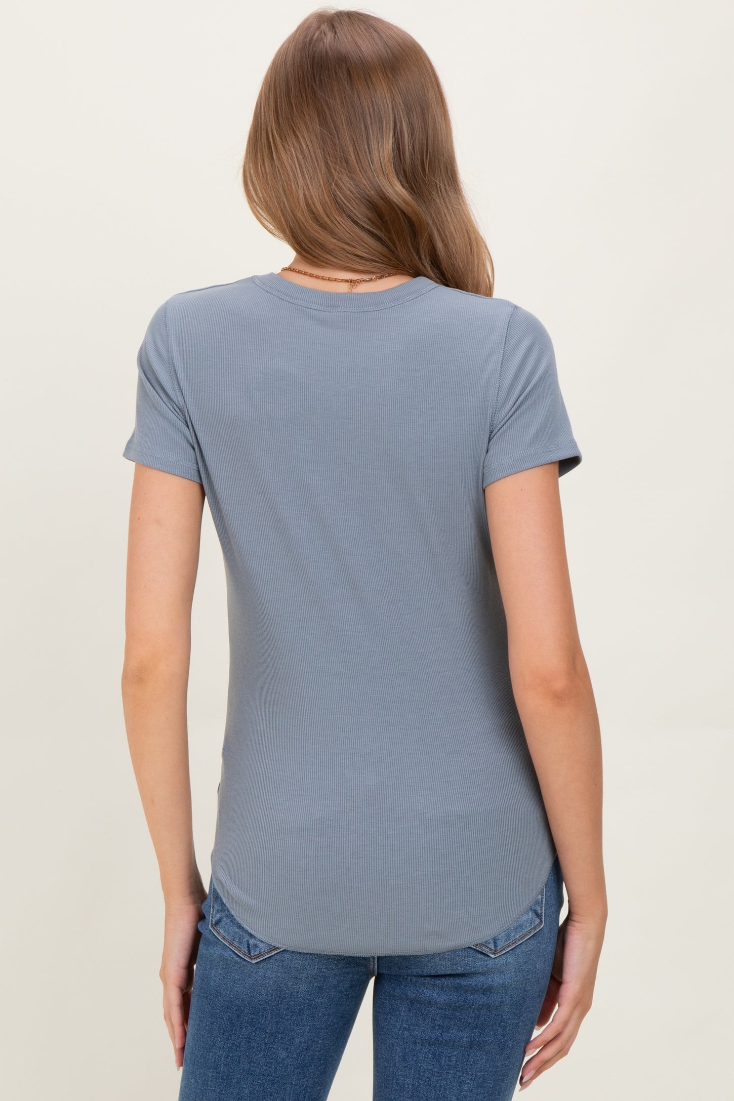 woman wearing a light gray maternity short sleeve top, viewed from the back, paired with blue jeans