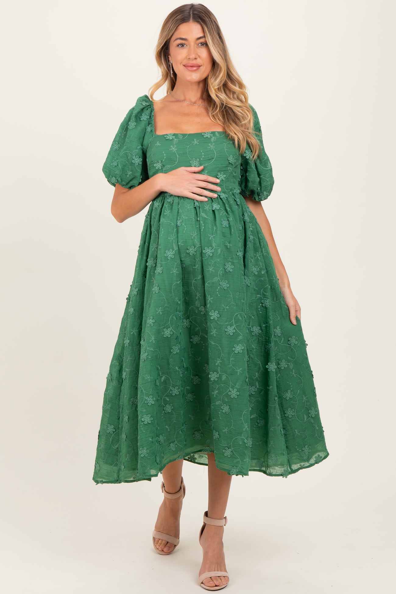 woman wearing a green puff sleeve maternity dress with floral details and holding her baby bump