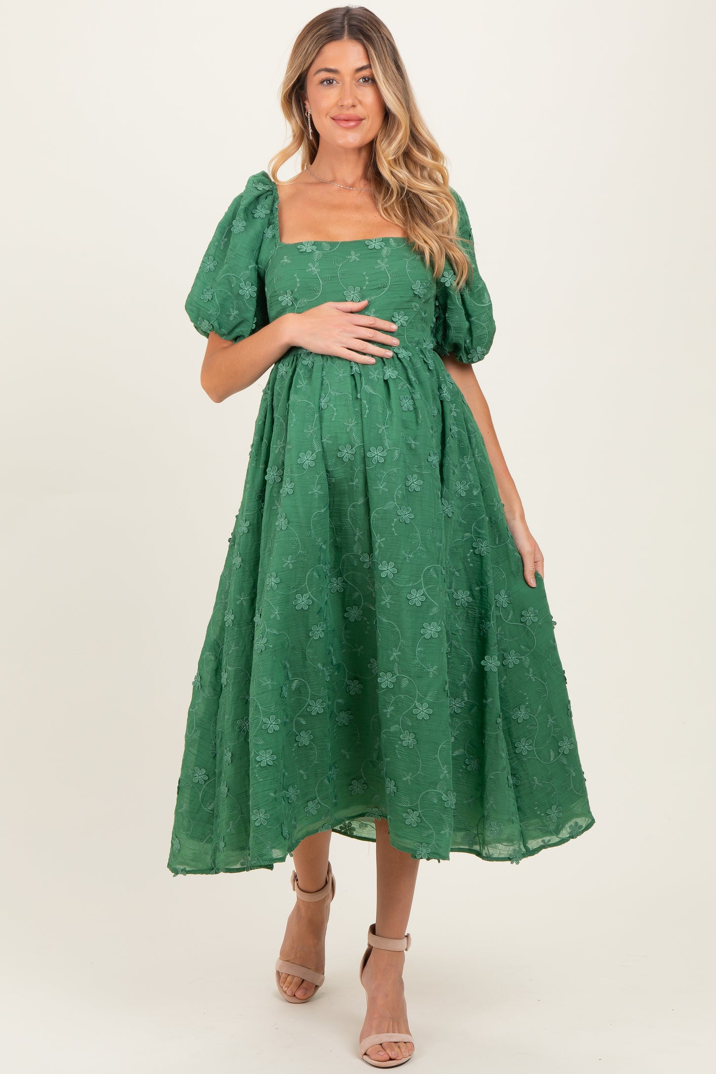 woman wearing a green puff sleeve maternity dress with floral details and holding her baby bump
