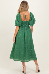 woman wearing a green maternity dress with puff sleeves and a smocked back, showing off her baby bump