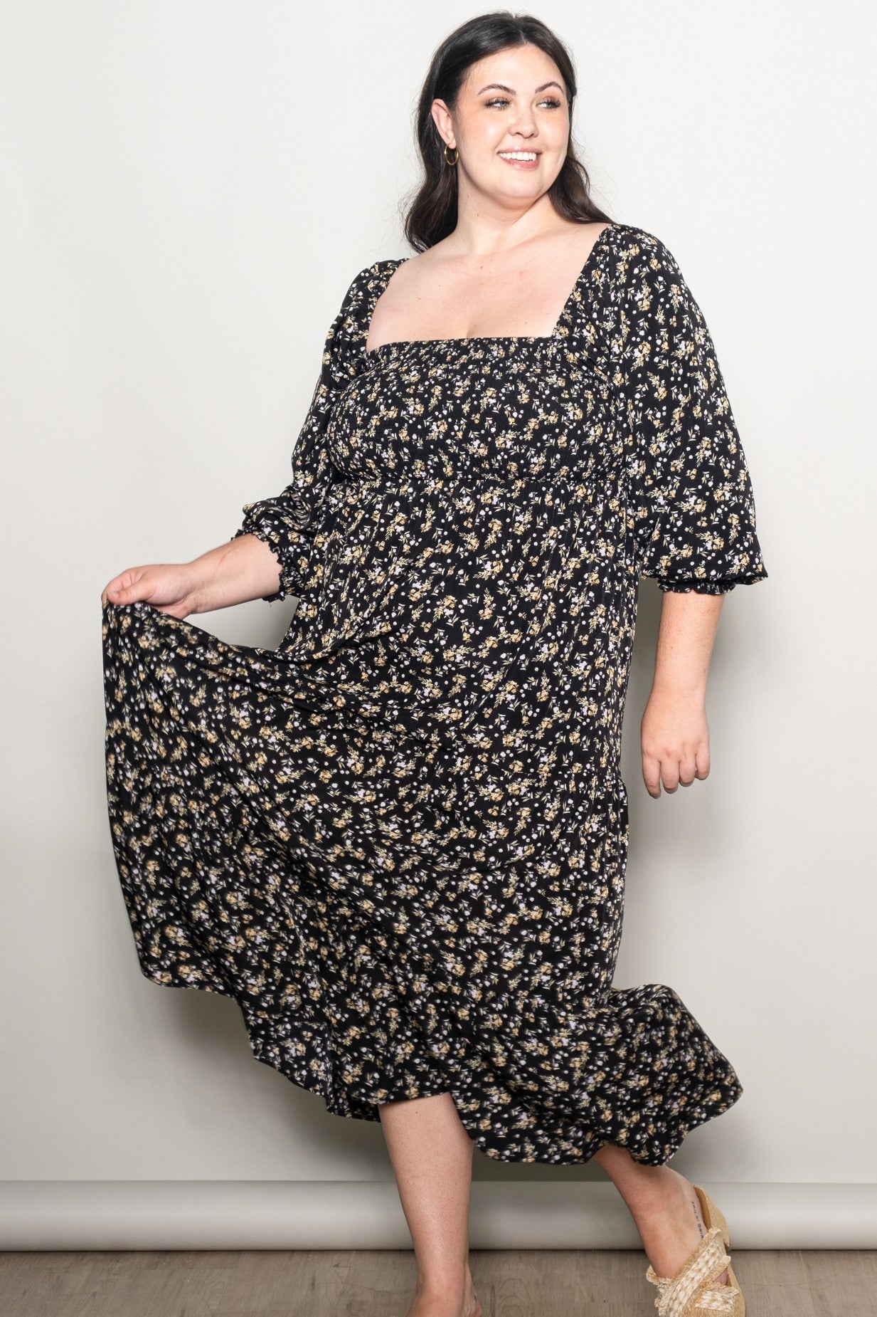 woman wearing a black floral plus-size maxi dress with a square neckline and puff sleeves, twirling gracefully