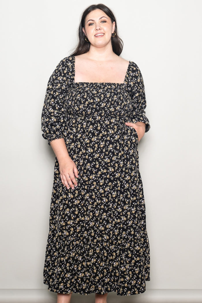 woman wearing a black floral maxi dress with puff sleeves and a square neckline, smiling at the camera