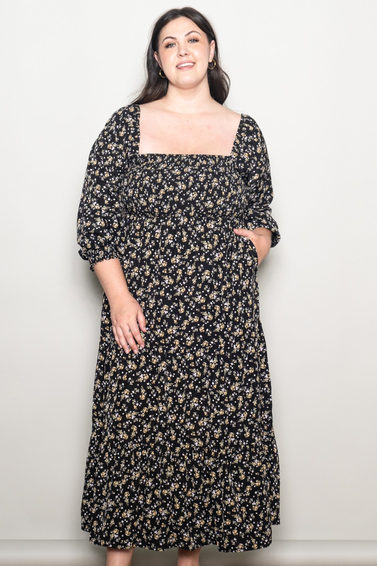 woman wearing a black floral maxi dress with puff sleeves and a square neckline, smiling at the camera