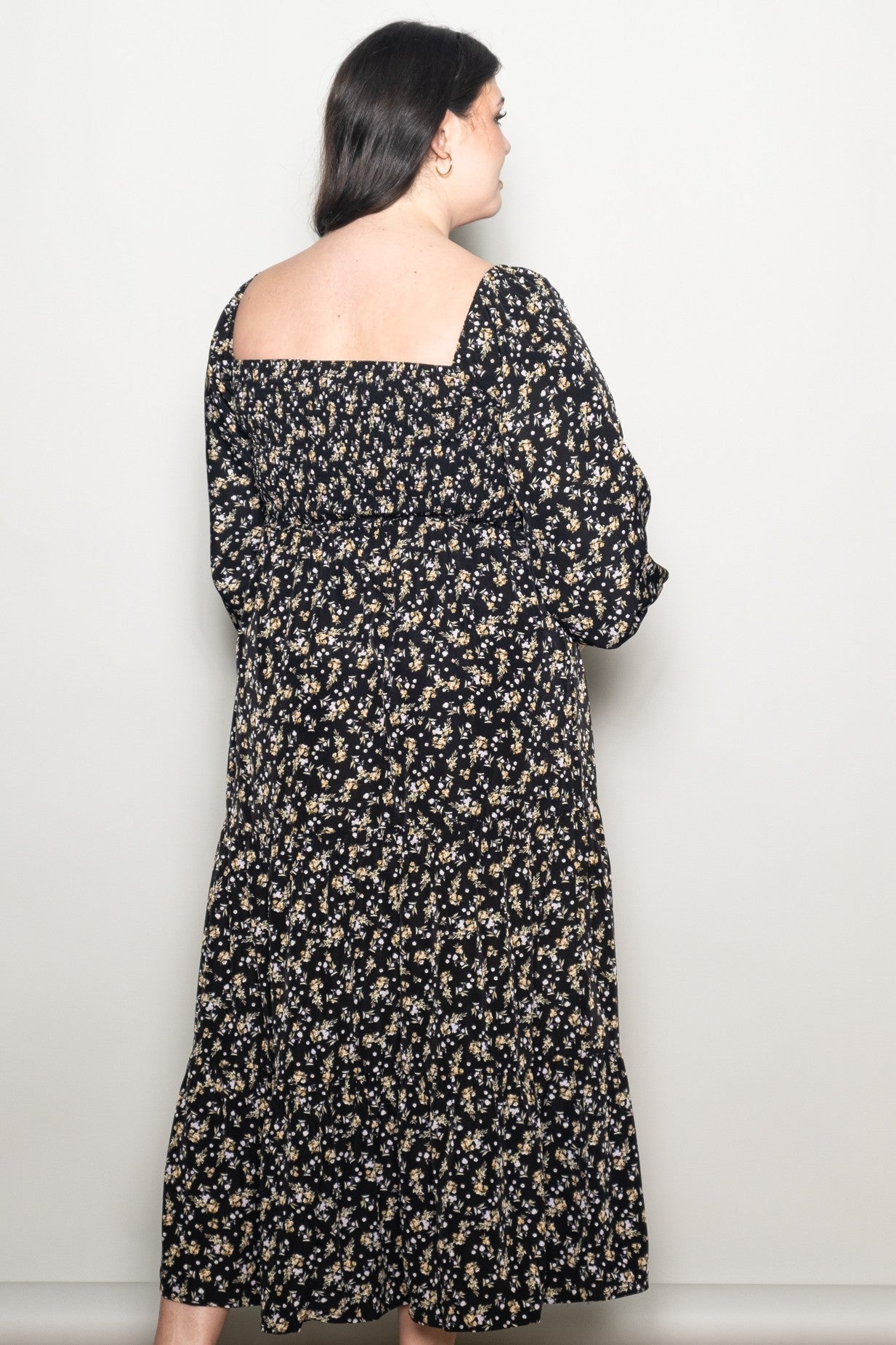 woman wearing a black floral plus size maxi dress with a square neckline and long sleeves, viewed from the back