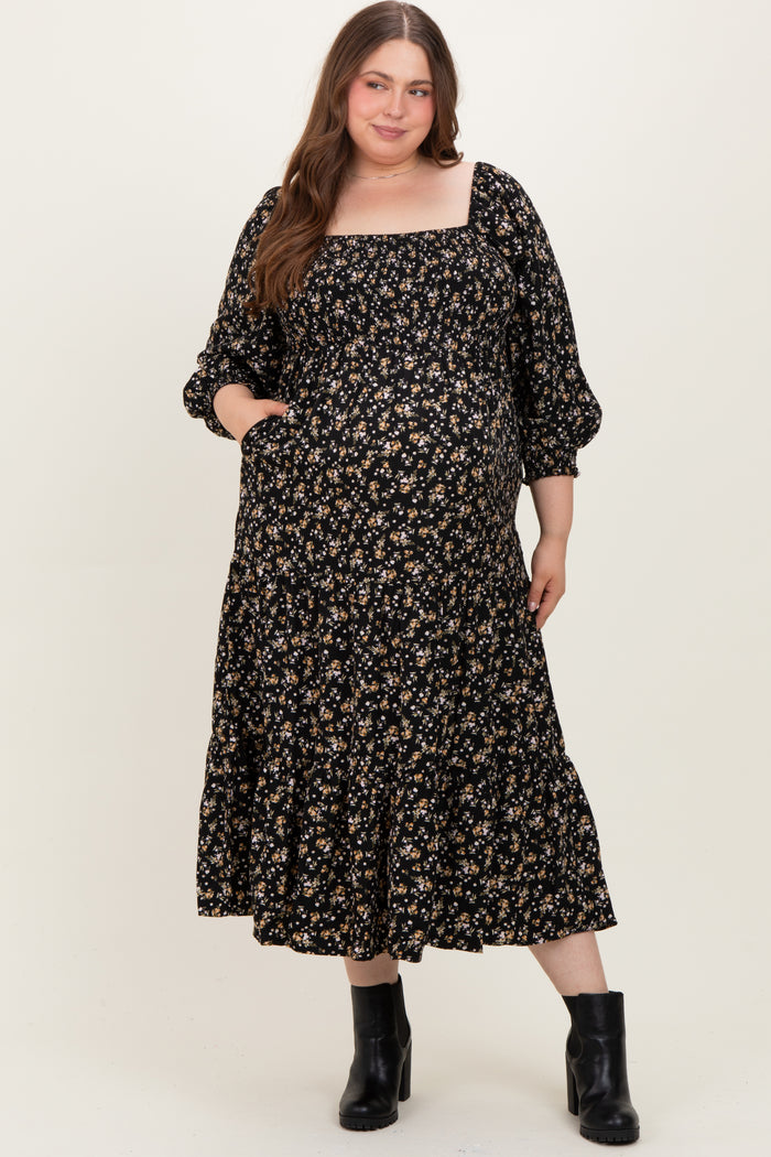 woman wearing a black floral maternity plus dress with a square neckline and puff sleeves, featuring a tiered skirt and pockets