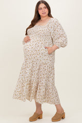 woman wearing a cream floral maternity dress with long puff sleeves and a tiered skirt, cradling her baby bump