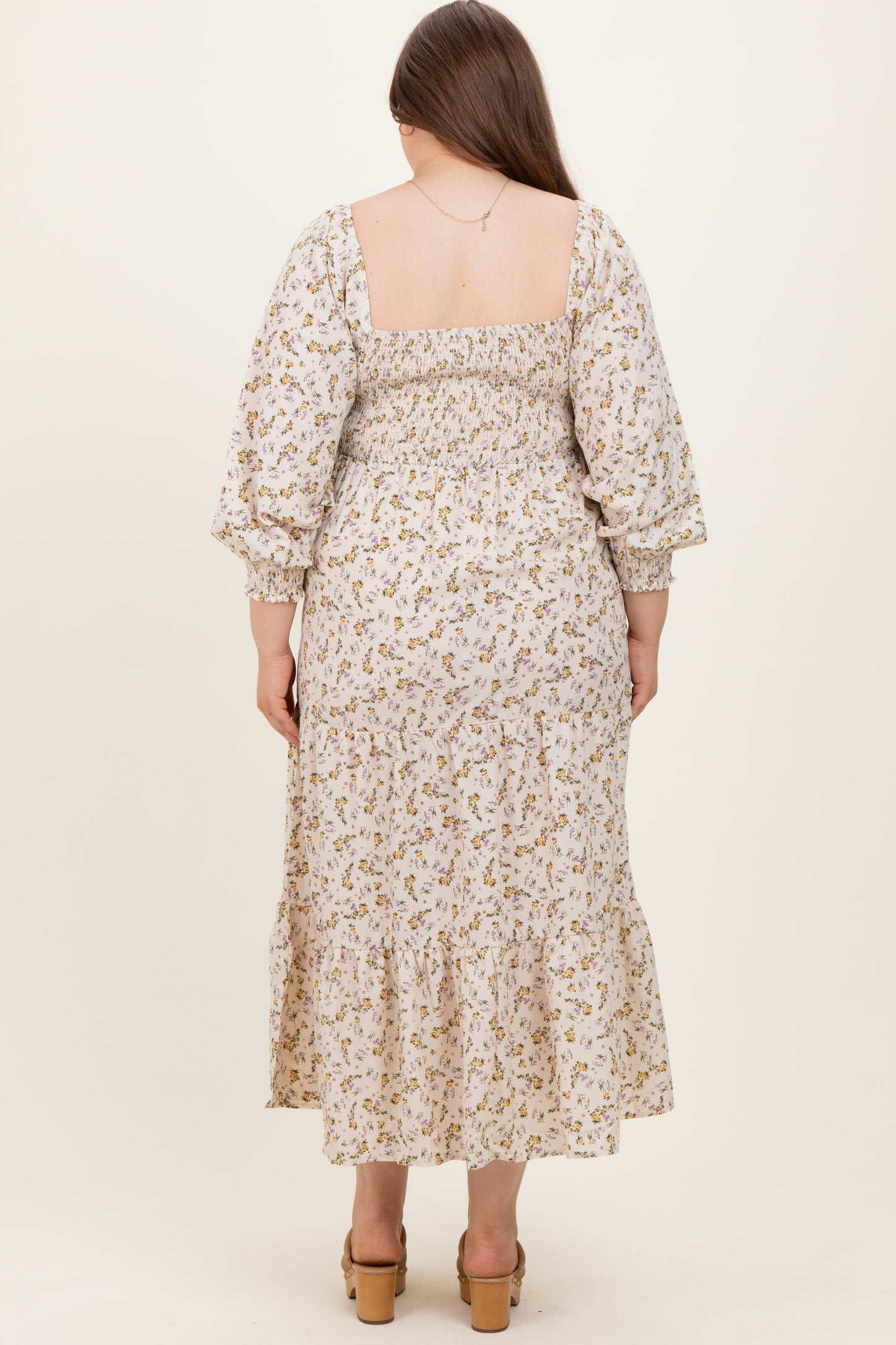 woman wearing a floral print maternity plus dress with a smocked back and tiered hem, shown from the back