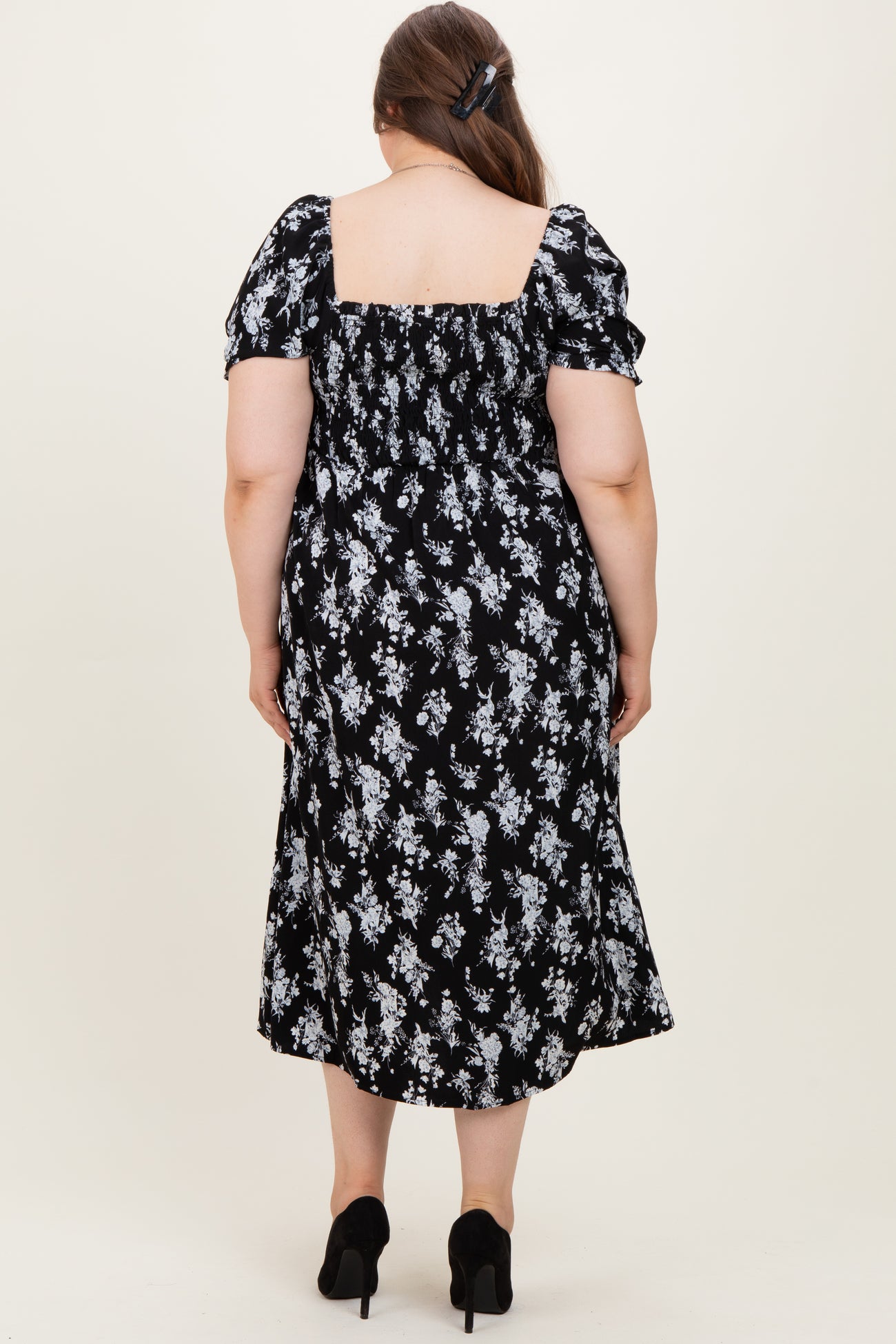 woman wearing a black floral maternity plus dress with puff sleeves and a square neckline, showing the back view