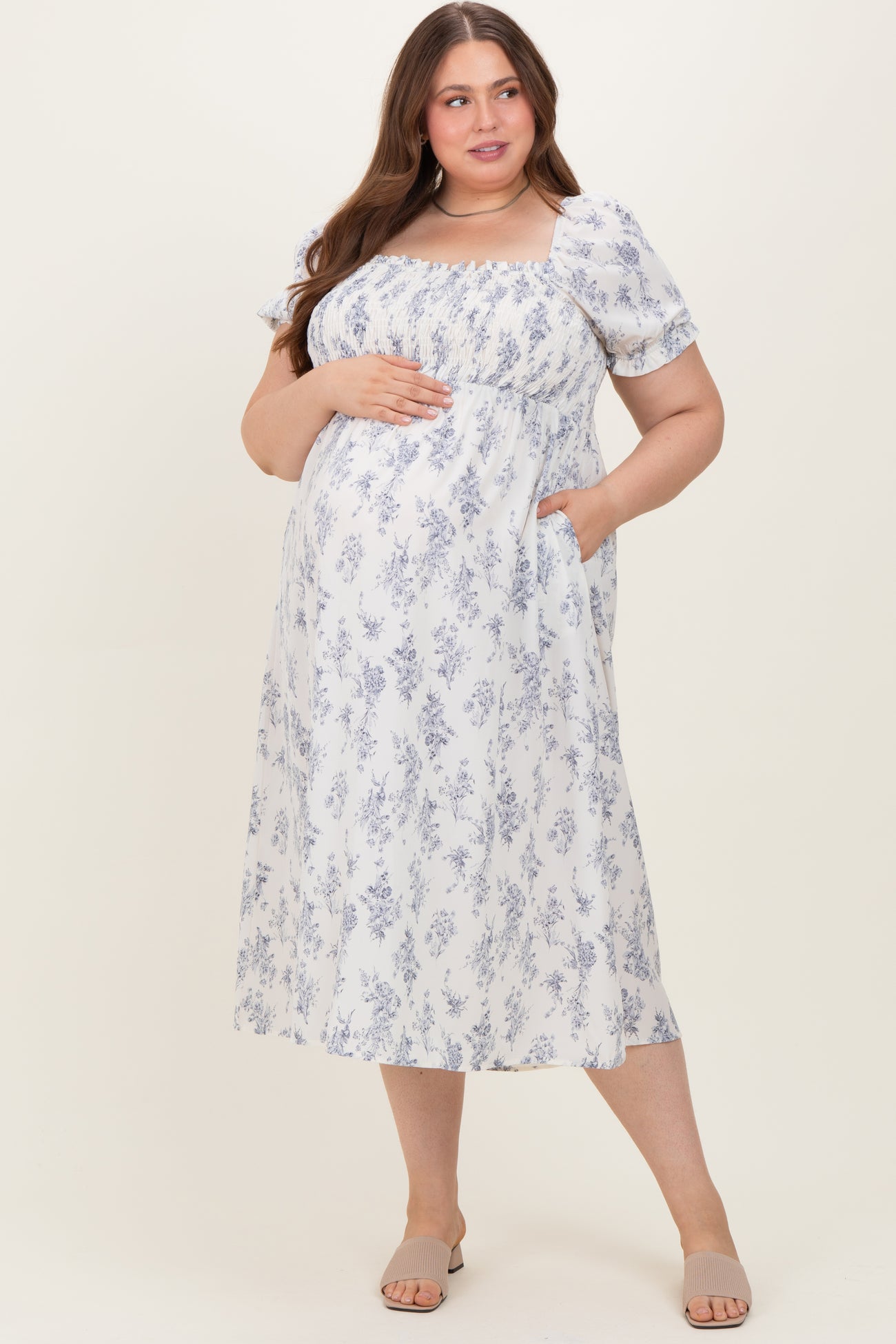 woman wearing a white floral print maternity plus midi dress and showing her baby bump, with puff sleeves and pockets