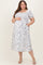 woman wearing a white floral print maternity plus midi dress and showing her baby bump, with puff sleeves and pockets