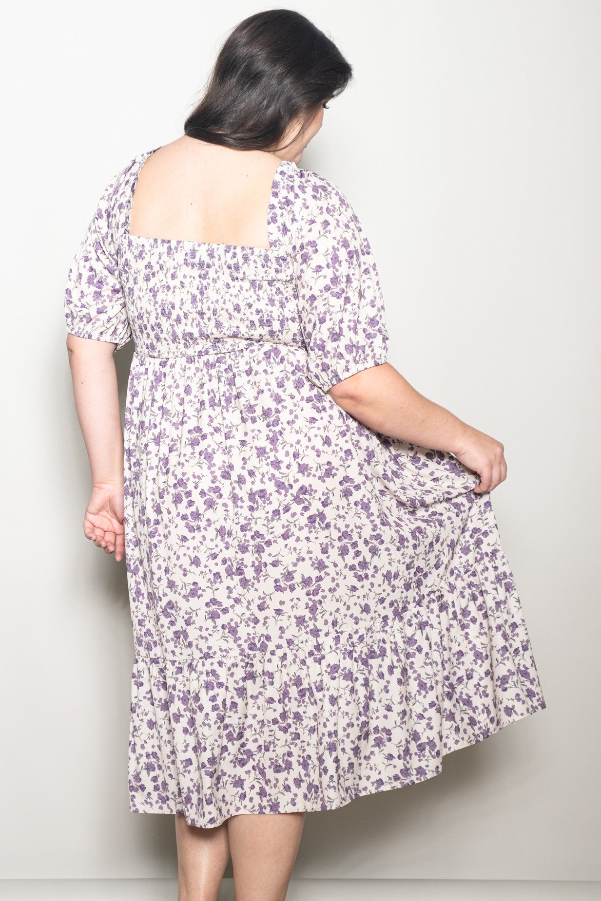 woman wearing a plus-size cream and purple floral print dress with a smocked back and puff sleeves