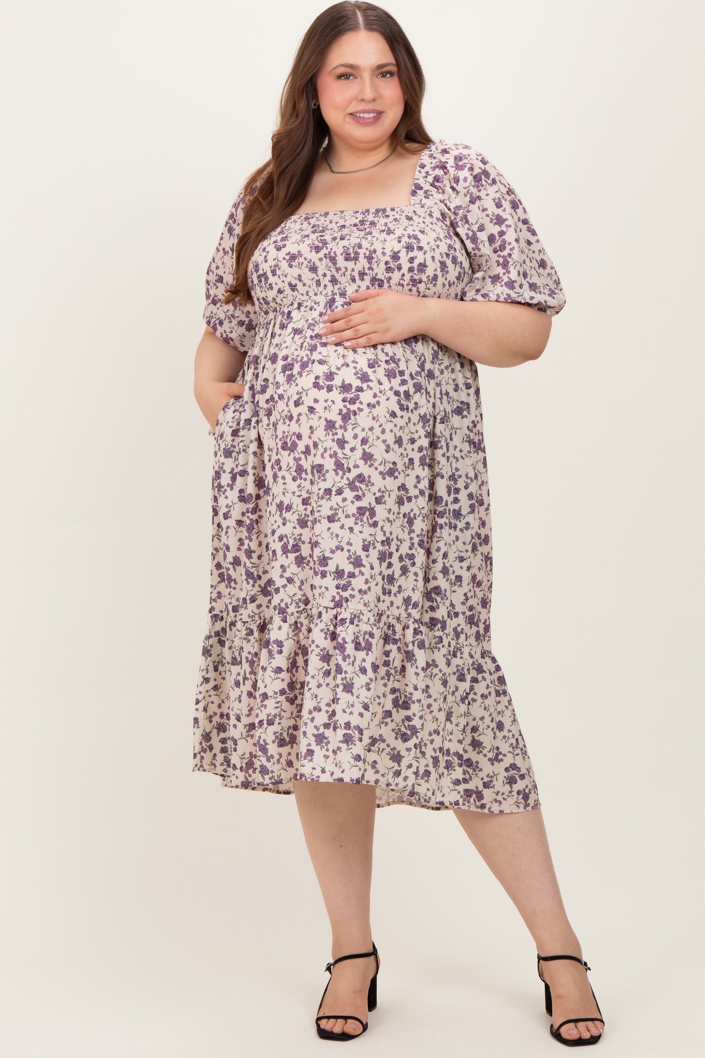 woman wearing a lavender floral maternity dress with short puff sleeves and a tiered skirt, showing a baby bump