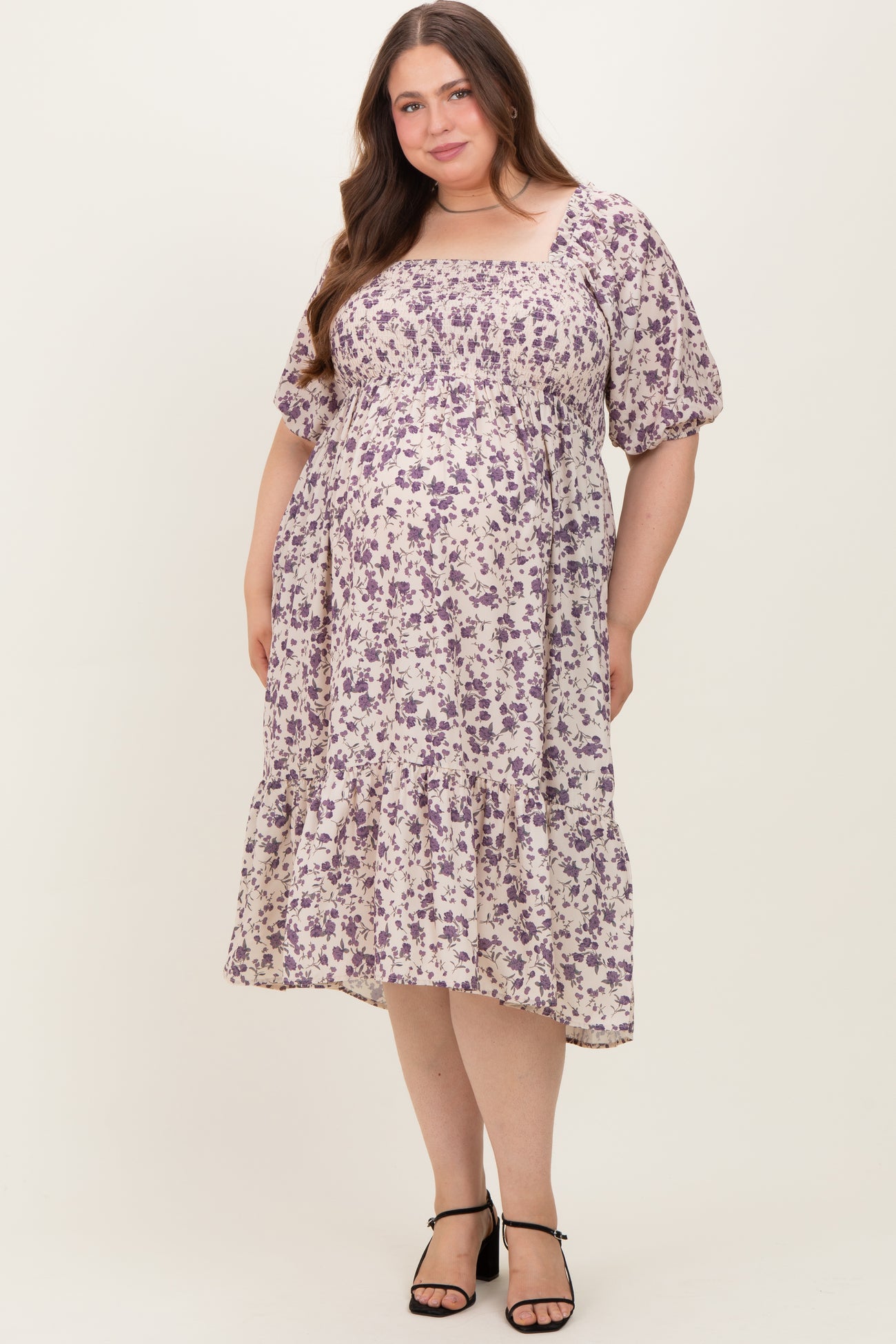 woman wearing a floral print maternity plus dress with a square neckline and puff sleeves, showing a visible baby bump