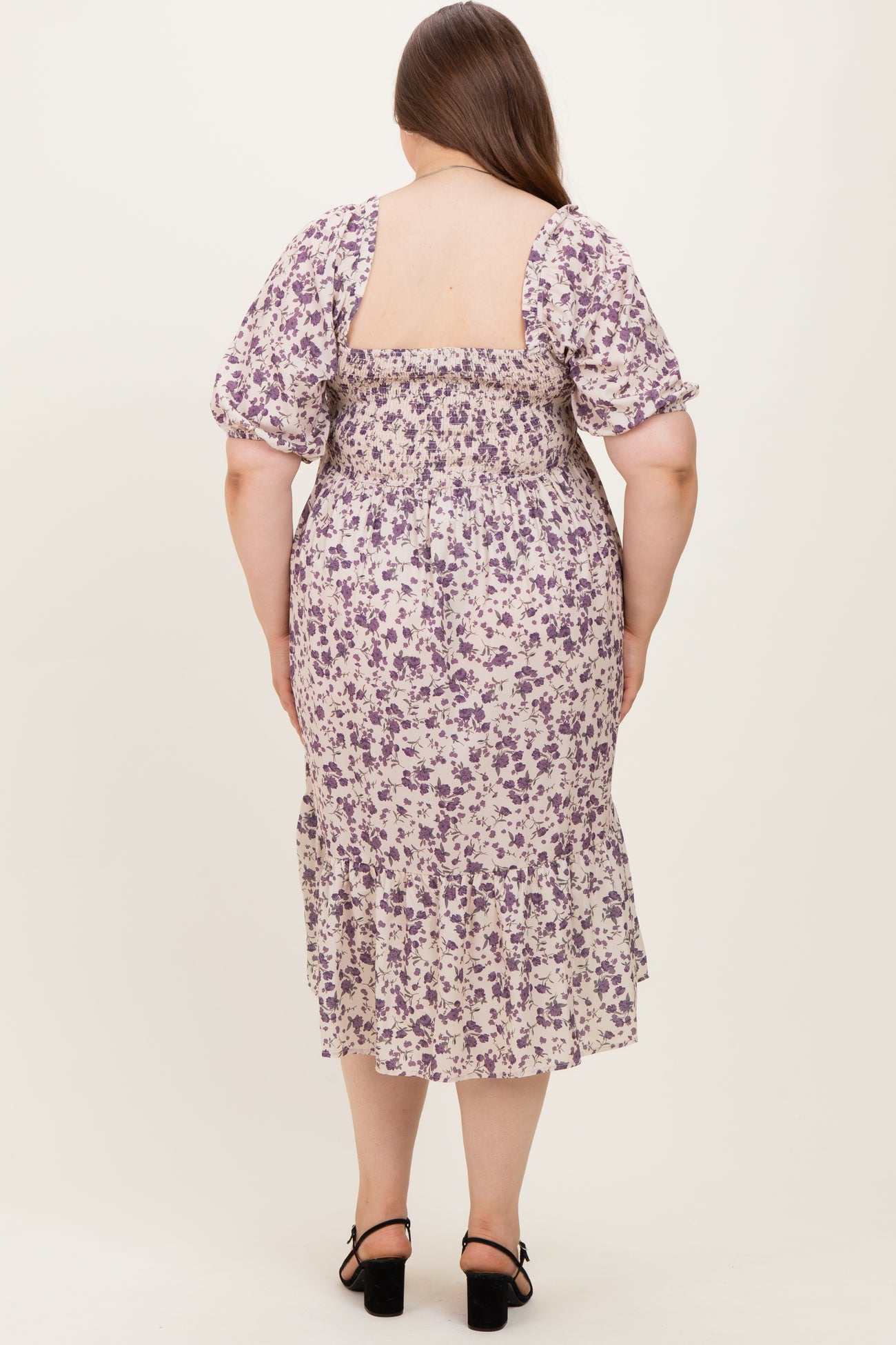 woman wearing a floral maternity plus dress with puff sleeves, featuring a smocked back and ruffled hem
