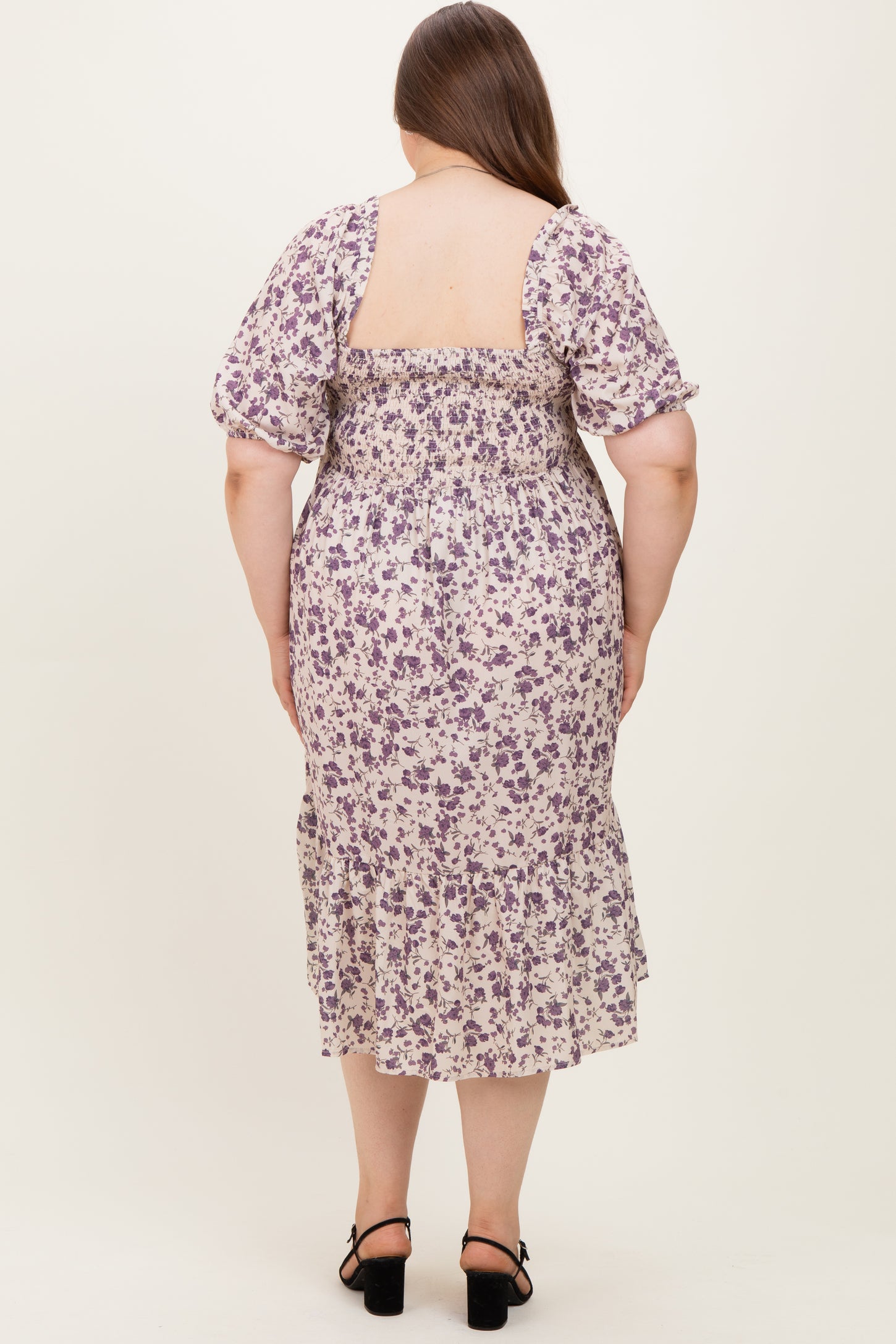woman wearing a floral maternity plus dress with puff sleeves, featuring a smocked back and ruffled hem