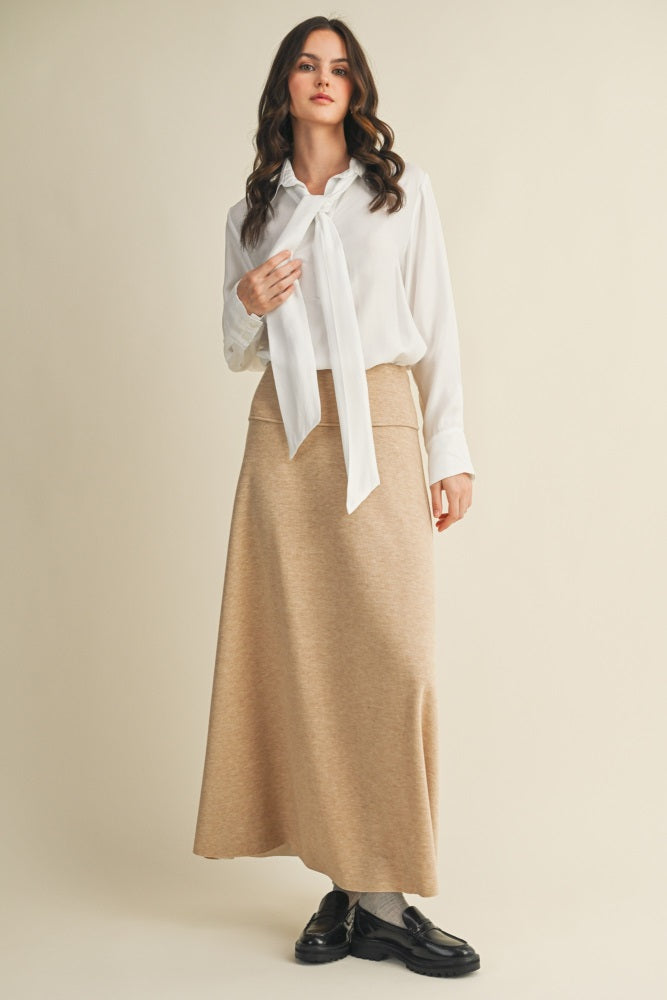 woman wearing a white long sleeve blouse with a tie detail and a beige maxi skirt, styled with black loafers