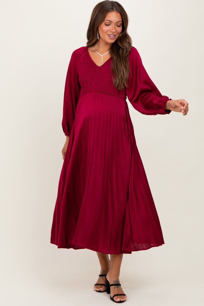woman wearing a burgundy maternity dress with a smocked bodice and pleated skirt, showcasing her baby bump