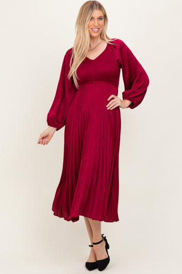 woman wearing a maroon pleated midi dress with a smocked bodice and long sleeves, styled with black heels