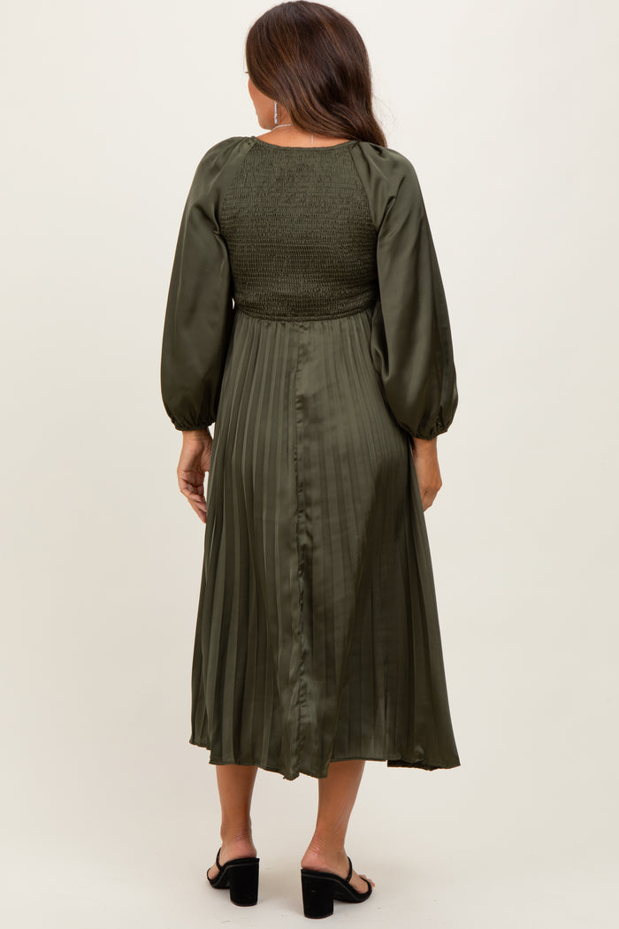 woman wearing a dark green maternity dress with smocked bodice and pleated skirt, showing a baby bump from behind