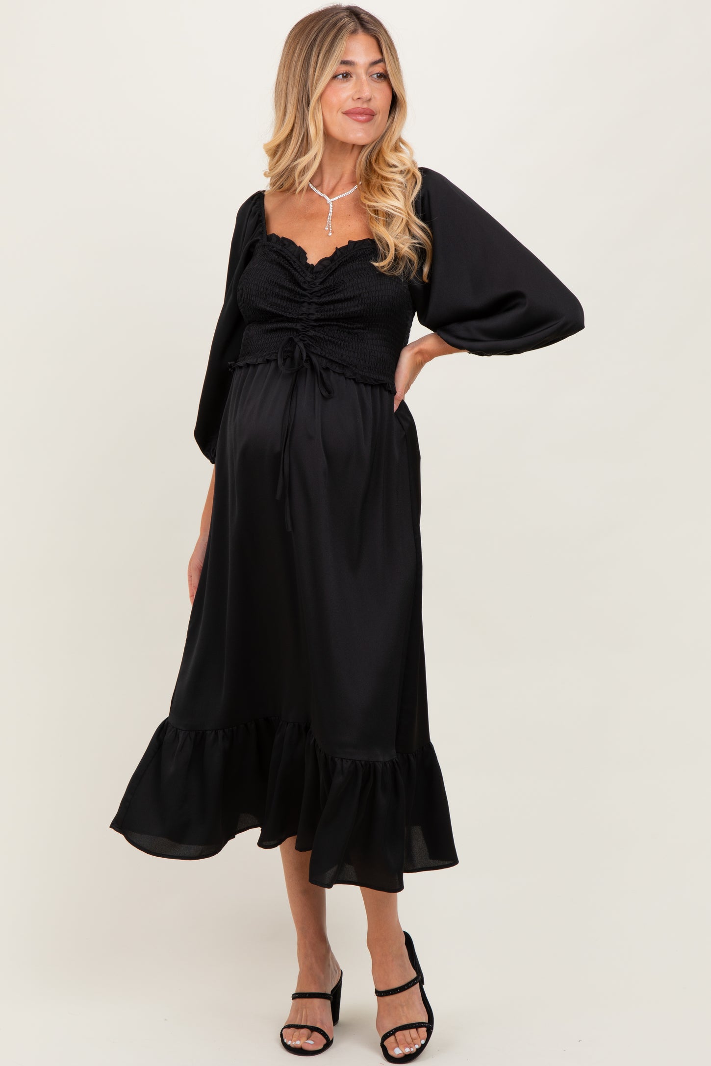 woman wearing a black maternity dress with puff sleeves and ruffle hem, showing her baby bump
