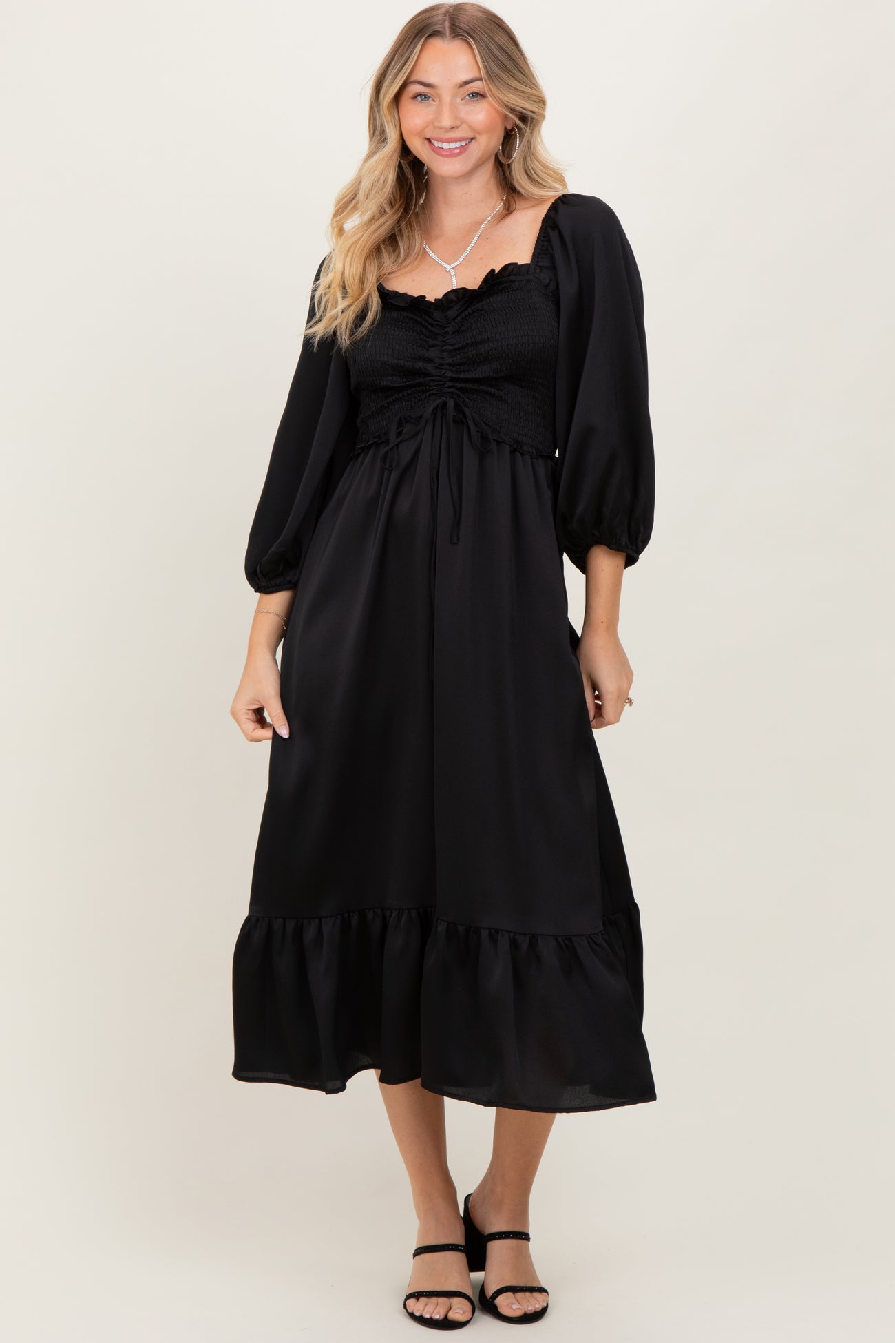 woman wearing a black maxi dress with puff sleeves and a ruffled hem, posing with a smile