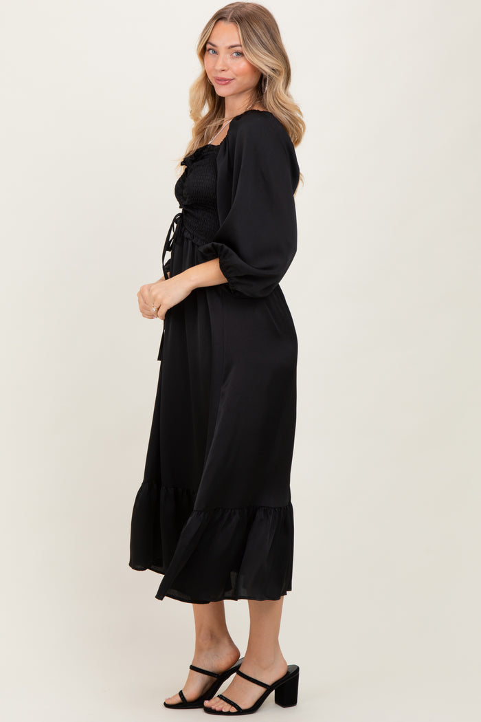 woman wearing a black smocked maxi dress with puff sleeves and a ruffled hem, posed sideways against a neutral background
