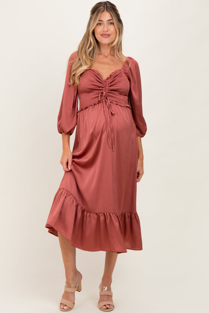 woman wearing a dusty rose maternity dress with a smocked bodice, long puff sleeves, and a ruffled hem